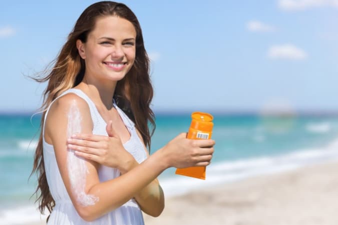 Pessoa aplicando protetor solar durante o verão como forma de prevenção ao câncer de pele